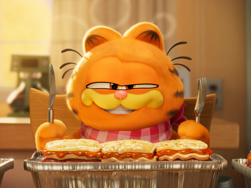 Garfield Animation, der Messer und Gabel in der Hand hält und vor einem Tisch mit Lasagne sitzt.