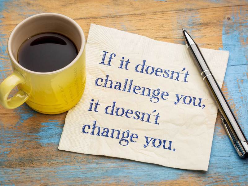 Gelbe Kaffeetasse neben einer Serviette auf einem Holztisch. Notitz auf Serviette: "If ist doen't challenge you, it doesn't change you."