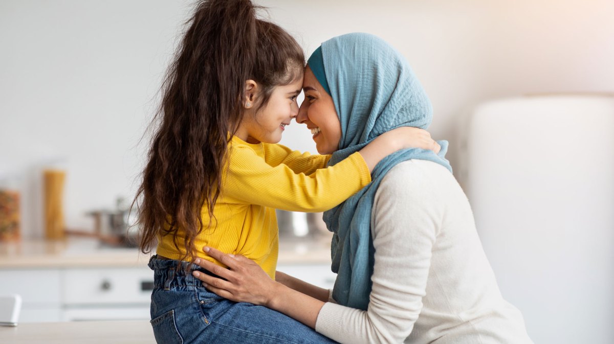 Mutter und Tochter sitzen sich gegenüber und berühren sich an der Stirn.