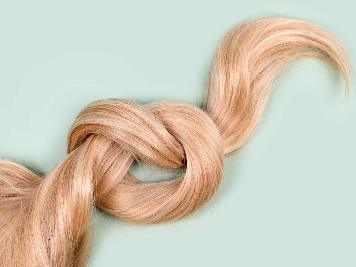 Blonde Haarsträhne zu einem Knoten gebunden. Strähne von honigblondem Haar auf mintfarbenem Hintergrund, Ansicht von oben. Friseur Service, Haar Stärke, Haarschnitt, Frisur, Färben oder Färben, Haarverlängerung, Behandlung Konzept.