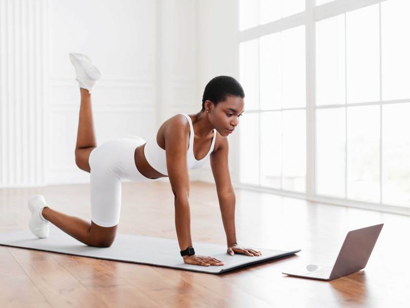 Fitnesstraining zu Hause: Sportliche Frau in weißer Trainingsbekleidung folgt einem Online-Fitness-Kurs in einem hellen Raum.