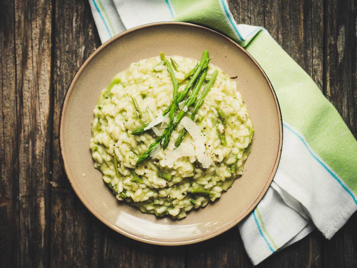 Cremiges Spargelrisotto mit geriebenem Parmesan auf einem braunen Teller, angerichtet auf einem dunklen Holztisch mit grün-weißer Serviette.