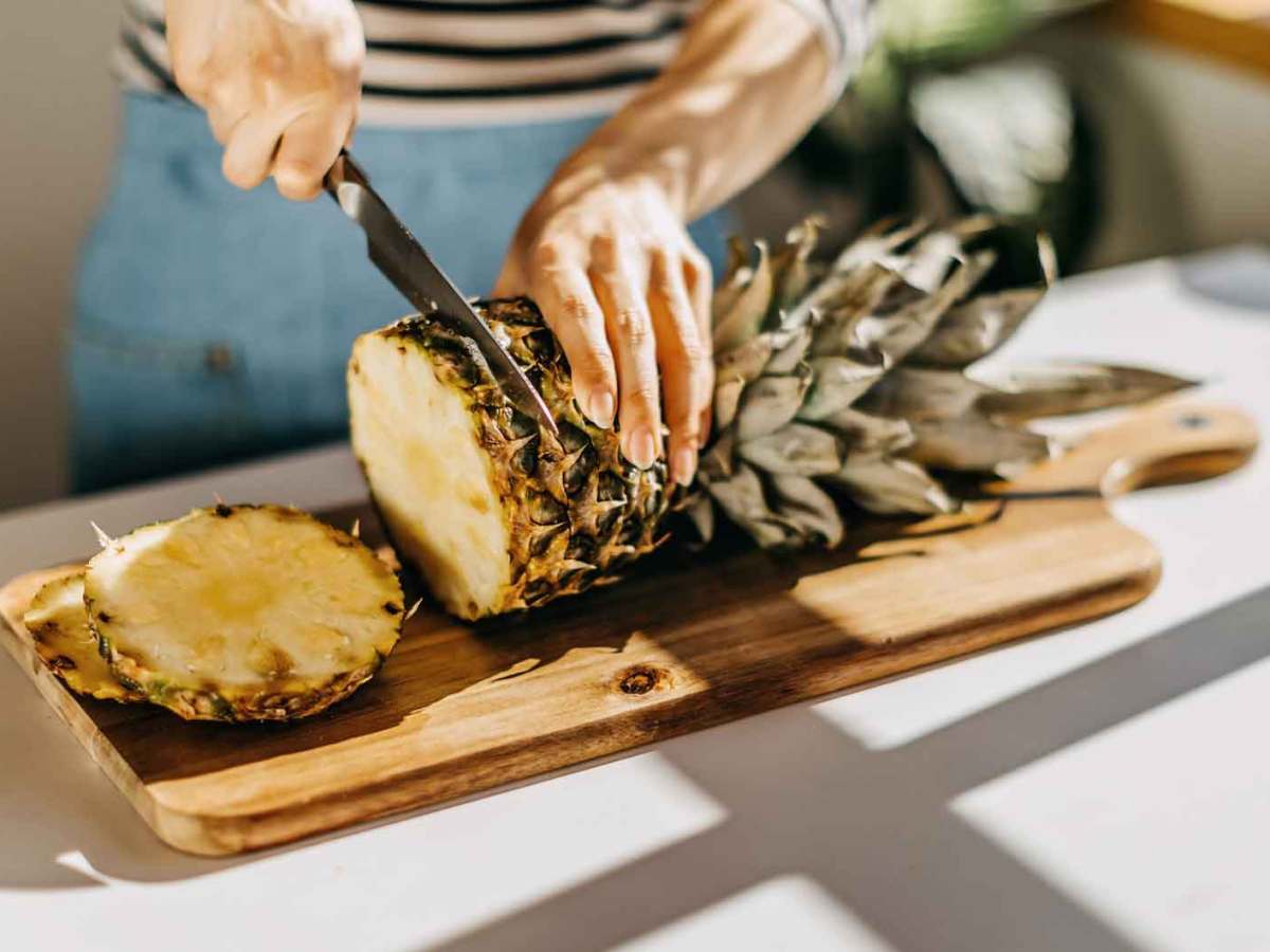 Frau schneidet eine Ananas auf einem Brett.