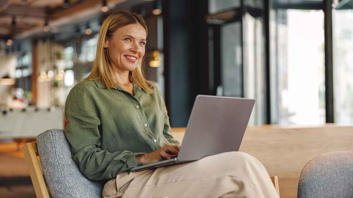 Junge Frau mit blonden Haaren sitzt bei der Arbeit mit einem Laptop.