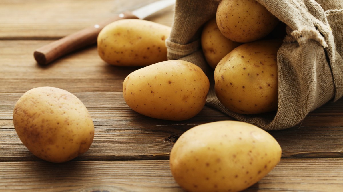 Rohe Kartoffeln liegen auf Holztisch, rollen aus Jutesack.