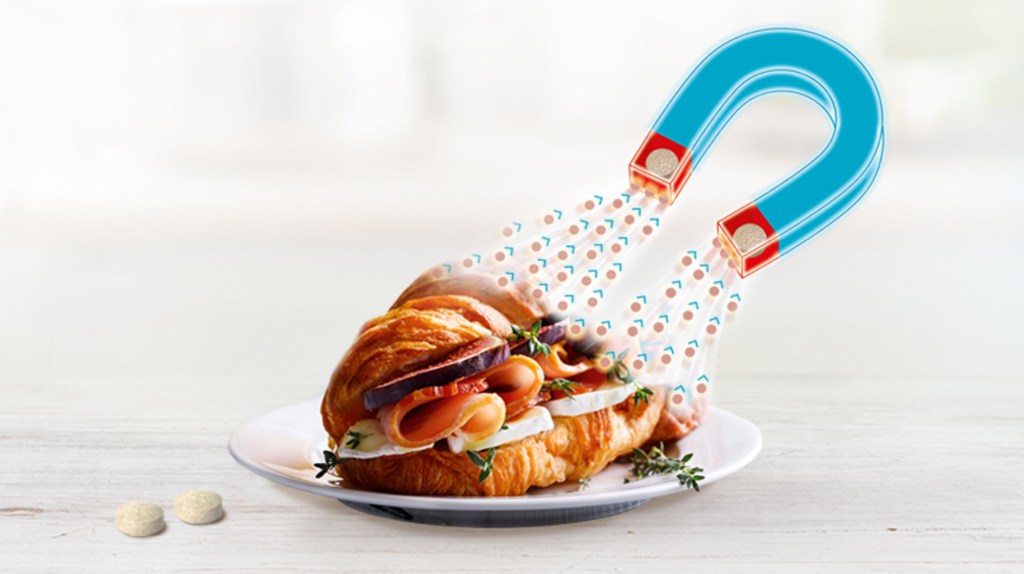 Auf einem weißen Teller liegt ein belegtes Croissant, das von einem animierten, blauen Hufeisenmagneten angezogen wird.