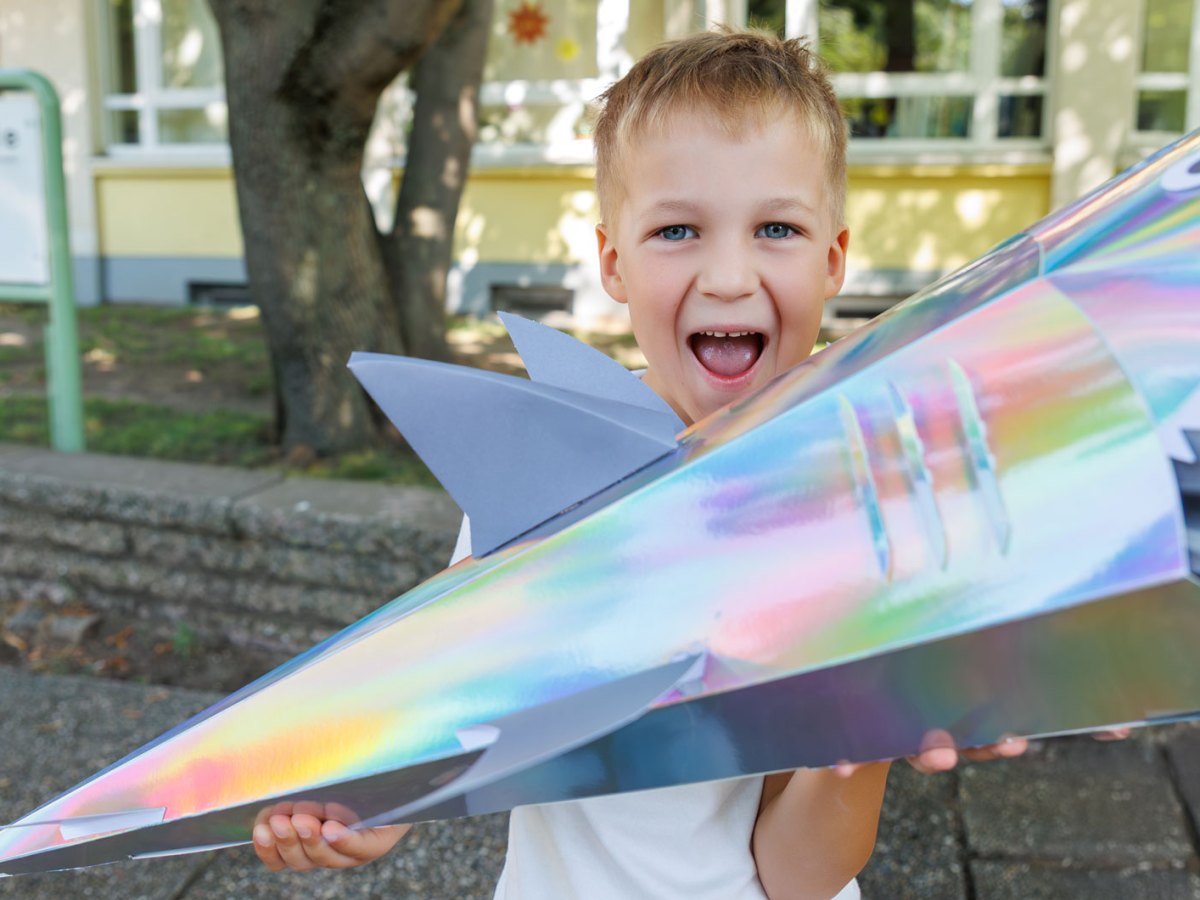 Junge an seinem ersten Schultag mit einer Schultüte in Hai-Form.