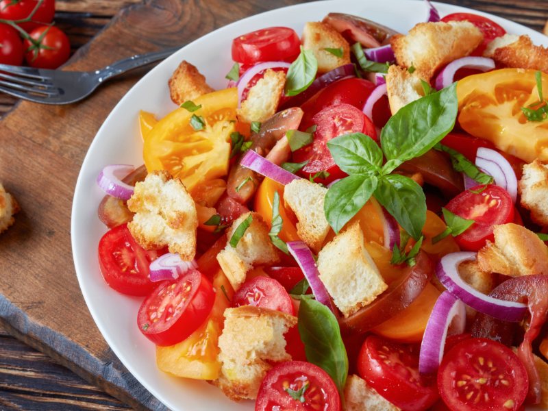 Brotsalat nach italienischer Art mit Tomaten, roten Zwiebeln und Basilikum in einer weißen Schüssel.