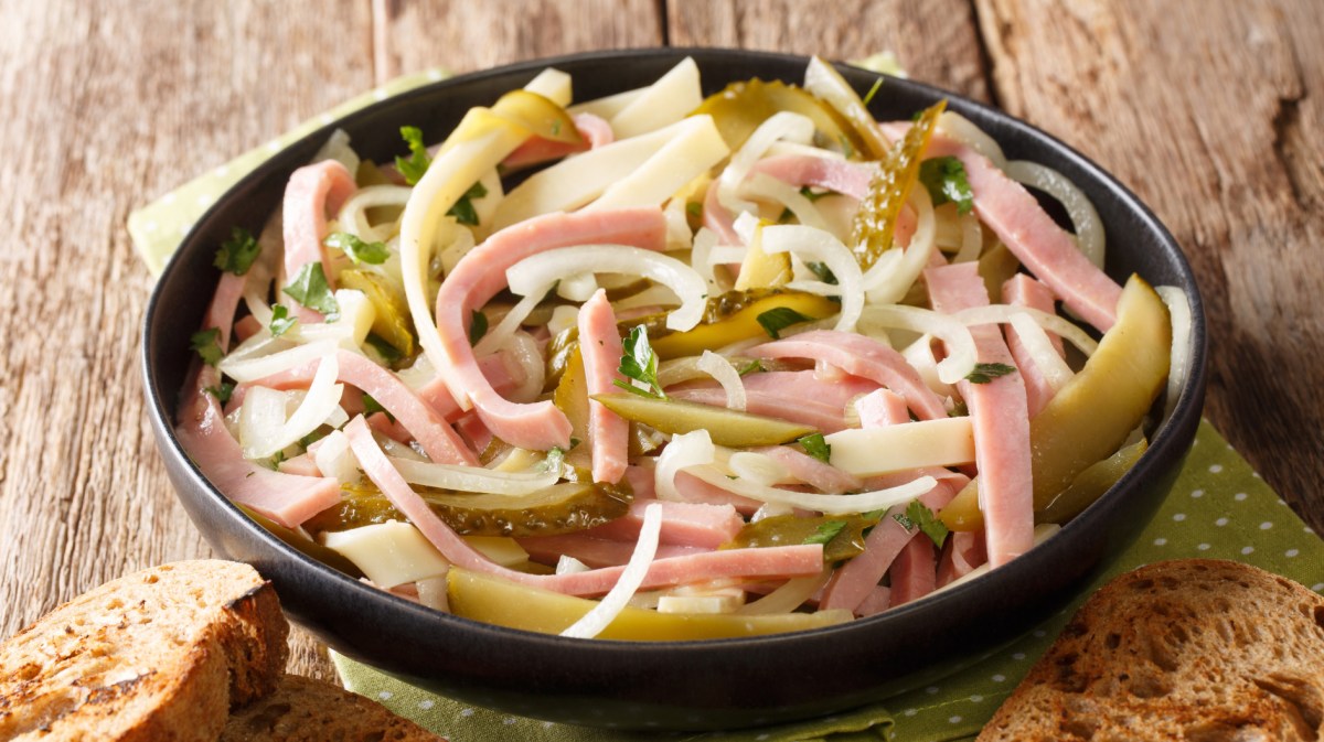 Wurstsalat mit Zwiebeln und Gurken in schwarzer Schüssel.