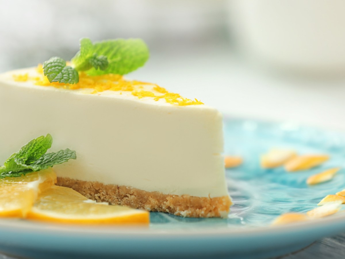 Frischkäse-Zitronen-Torte mit Keksboden auf einem türkisen Teller.