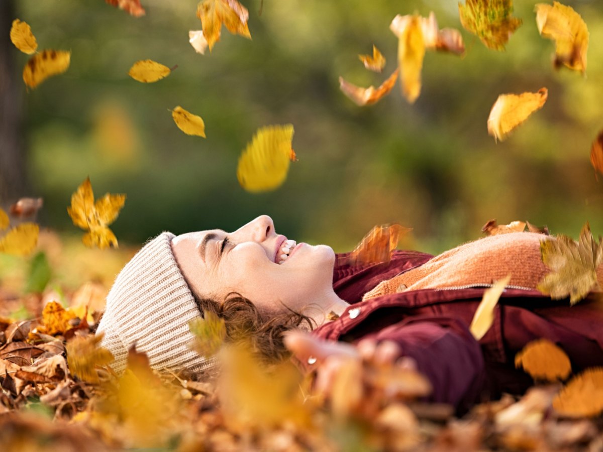 Frau mit Mütze liegt im Herbstlaub