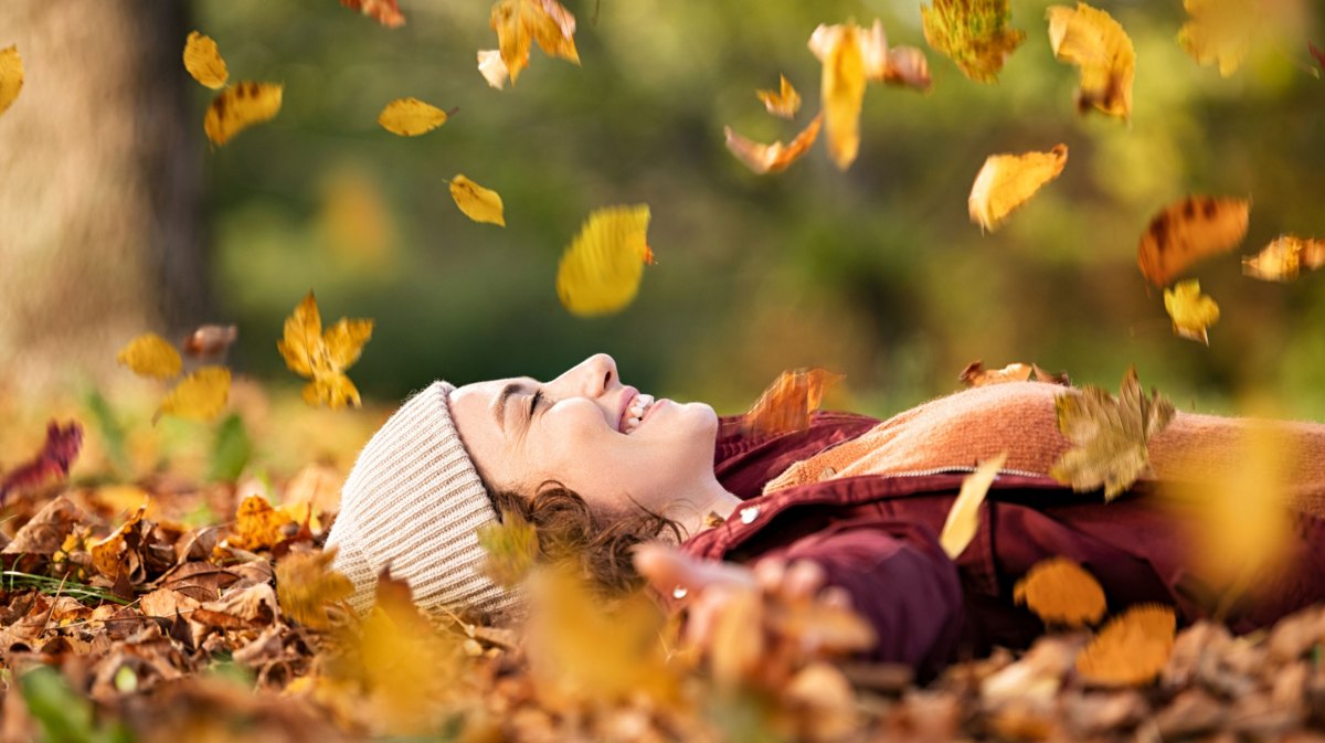 Frau mit Mütze liegt im Herbstlaub