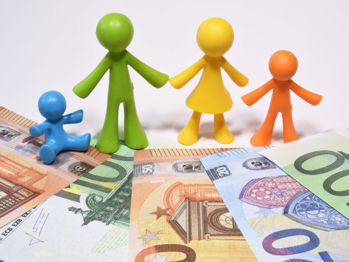 Plasikfiguren, die Mutter, Vater und zwei Kinder darstellen, stehen auf ein paar Euroscheinen.