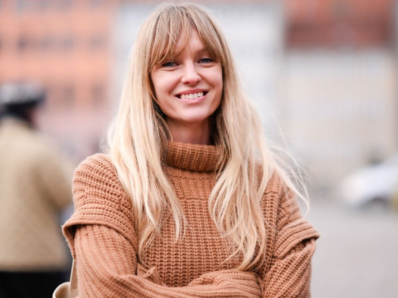Blonde Frau mit hellbraunem Pullover lächelt in die Kamera.