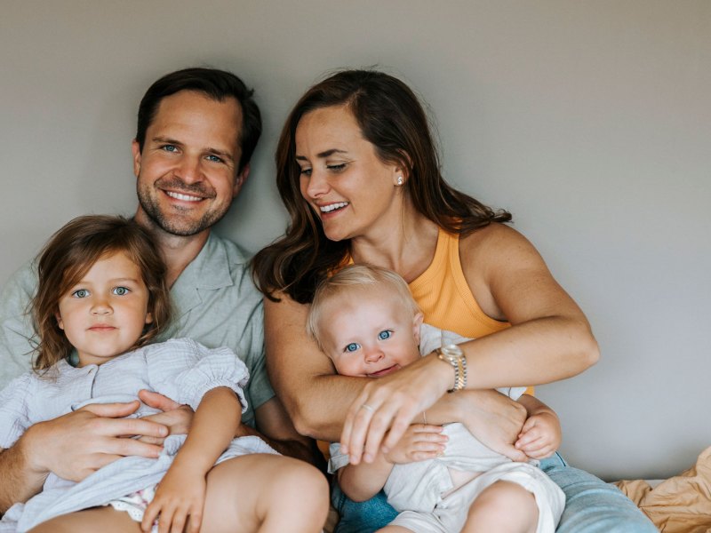 Familie aus Vater, Mutter und zwei Kindern kuscheln auf Bett