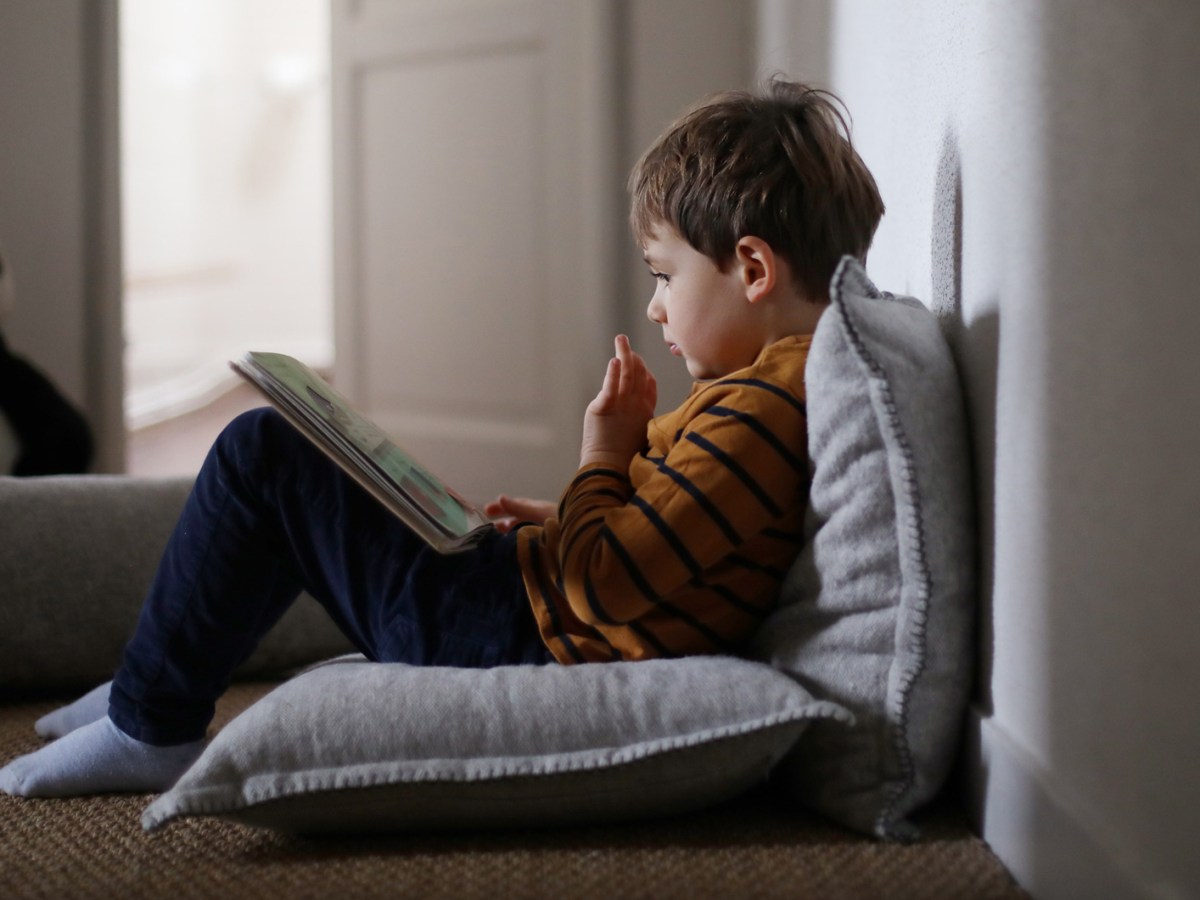 Vierjähriger sitzt auf dem Fußboden und schaut sich ein Buch an.