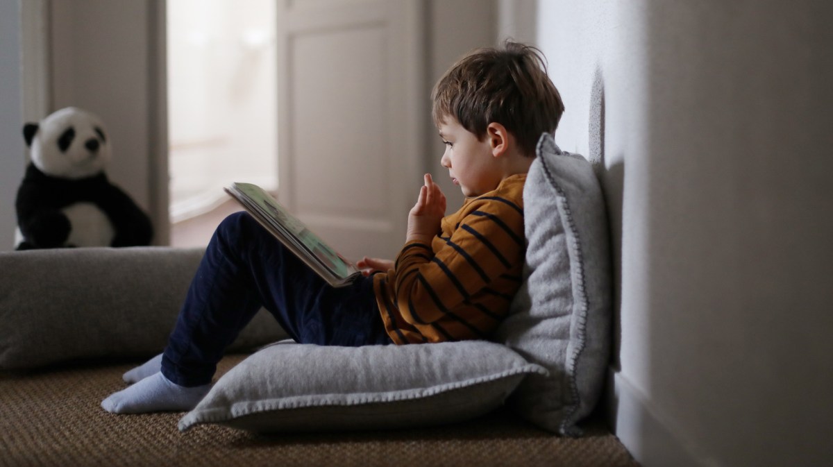Vierjähriger sitzt auf dem Fußboden und schaut sich ein Buch an.