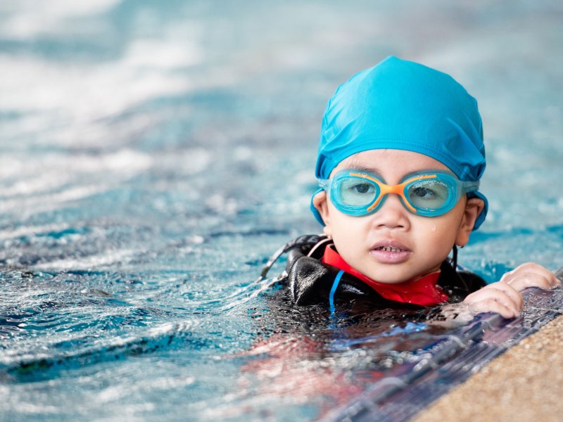 Kleines Mädchen mit Badekappe und Schwimmbrille im Schwimmbecken.