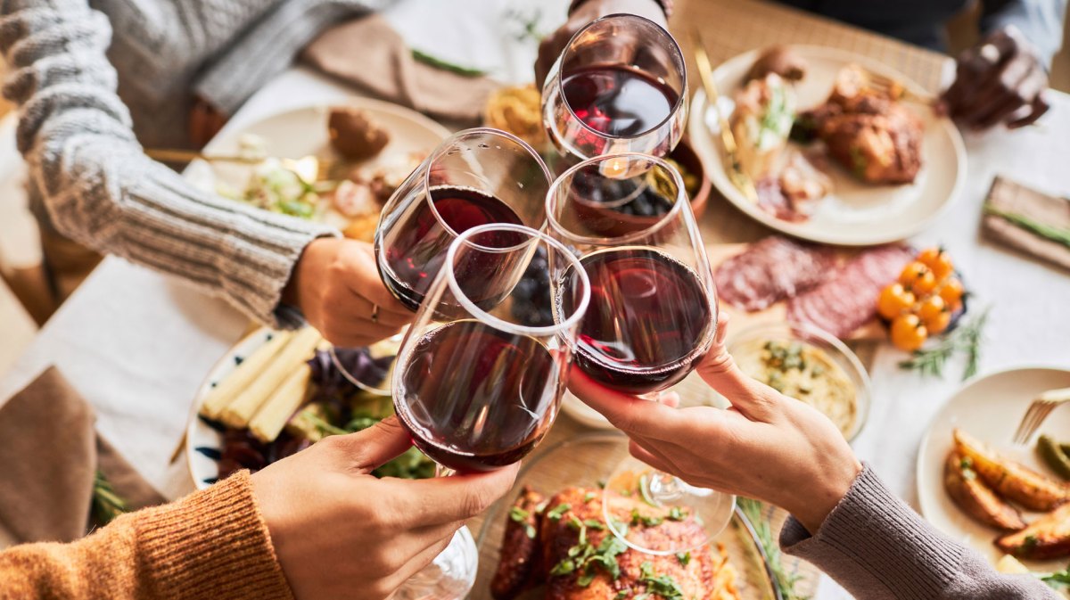 Nahaufnahme einer Gruppe, die mit Gläsern mit Rotwein anstößt.