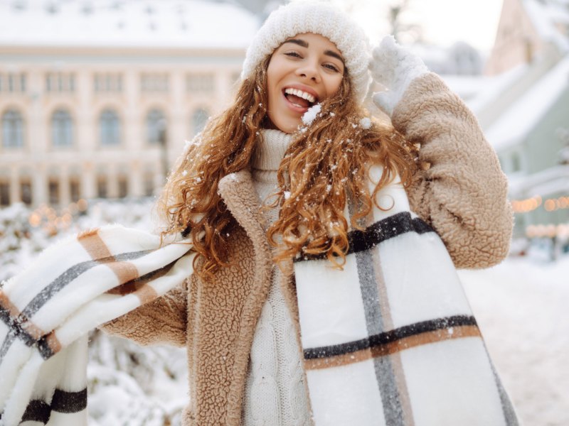 Frau in Winterkleidung in einer verschneiten Stadt lächelt in die Kamera