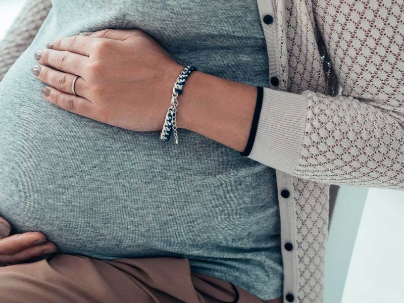 Nahaufnahme von Frauenhänden, die auf dem Schwangerschaftsbauch liegen.