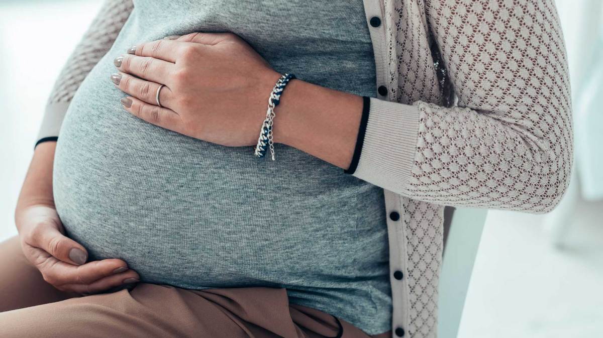 Nahaufnahme von Frauenhänden, die auf dem Schwangerschaftsbauch liegen.