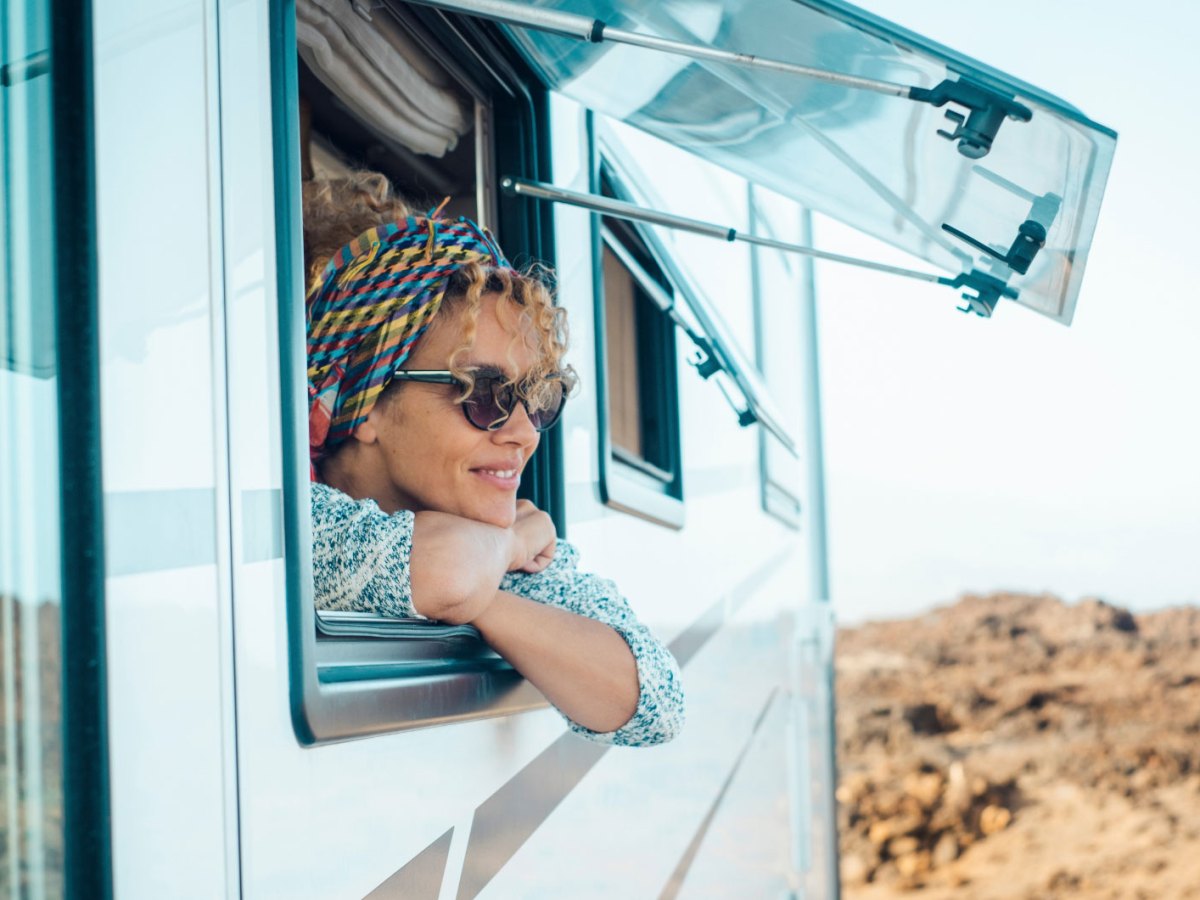 Frau mit Sonnenbrille schaut aus offenem Fenster eines Wohnmobils