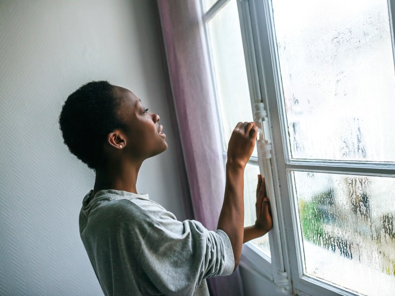 Dunkelhäutige Frau öffnen beschlagenes Fenster im Winter