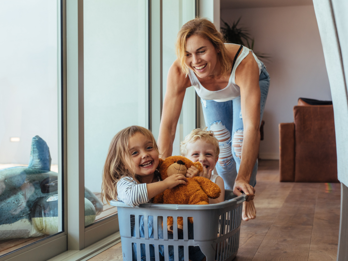Eine Mutter schiebt ihren kleinen Sohn und ihre kleine Tochter in einem Wäschekorb durch die Wohnung