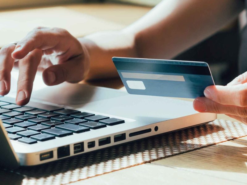 Frau tippt mit einer Hand auf dem Laptop und hält in der anderen Hand ihre Bankkarte.