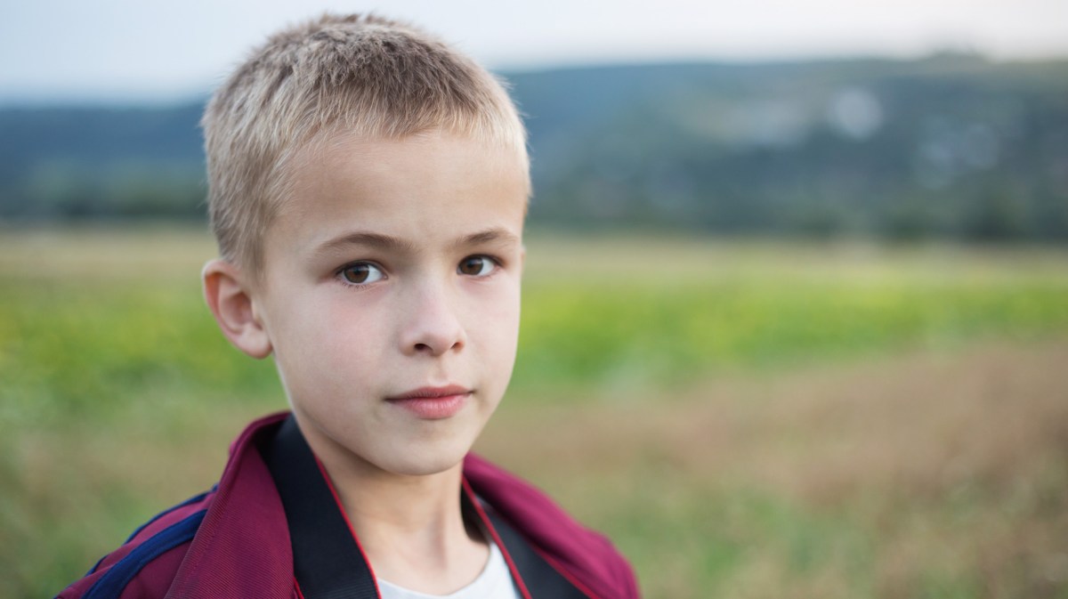 Porträt eines Jungen, ca. 10 Jahre alt, der draußen steht und ernst schaut.
