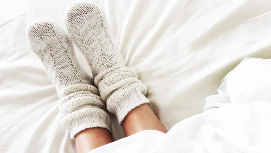 Füße in gestrickten Wollsocken auf Bett