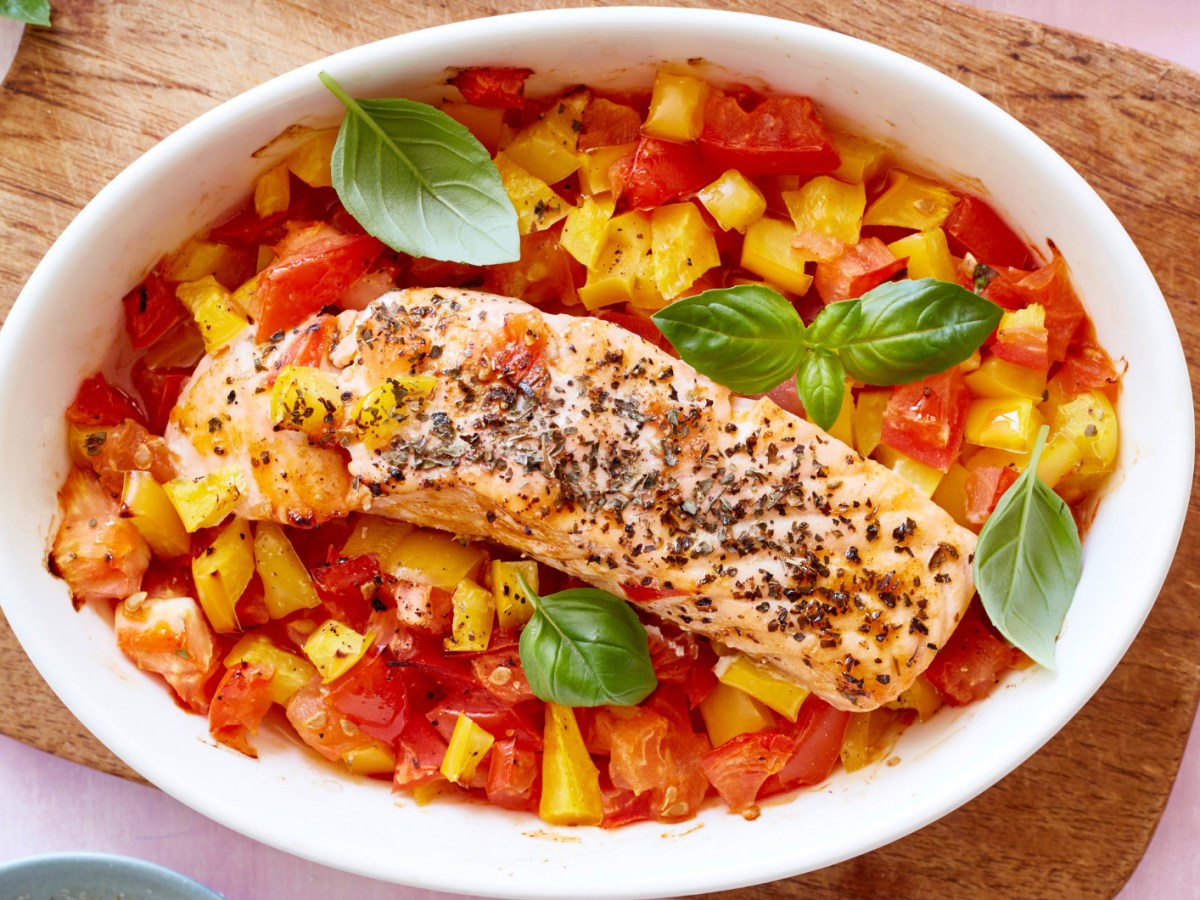 Lachs auf einem Bett aus Tomaten und Paprika in einer weißen Auflaufform.
