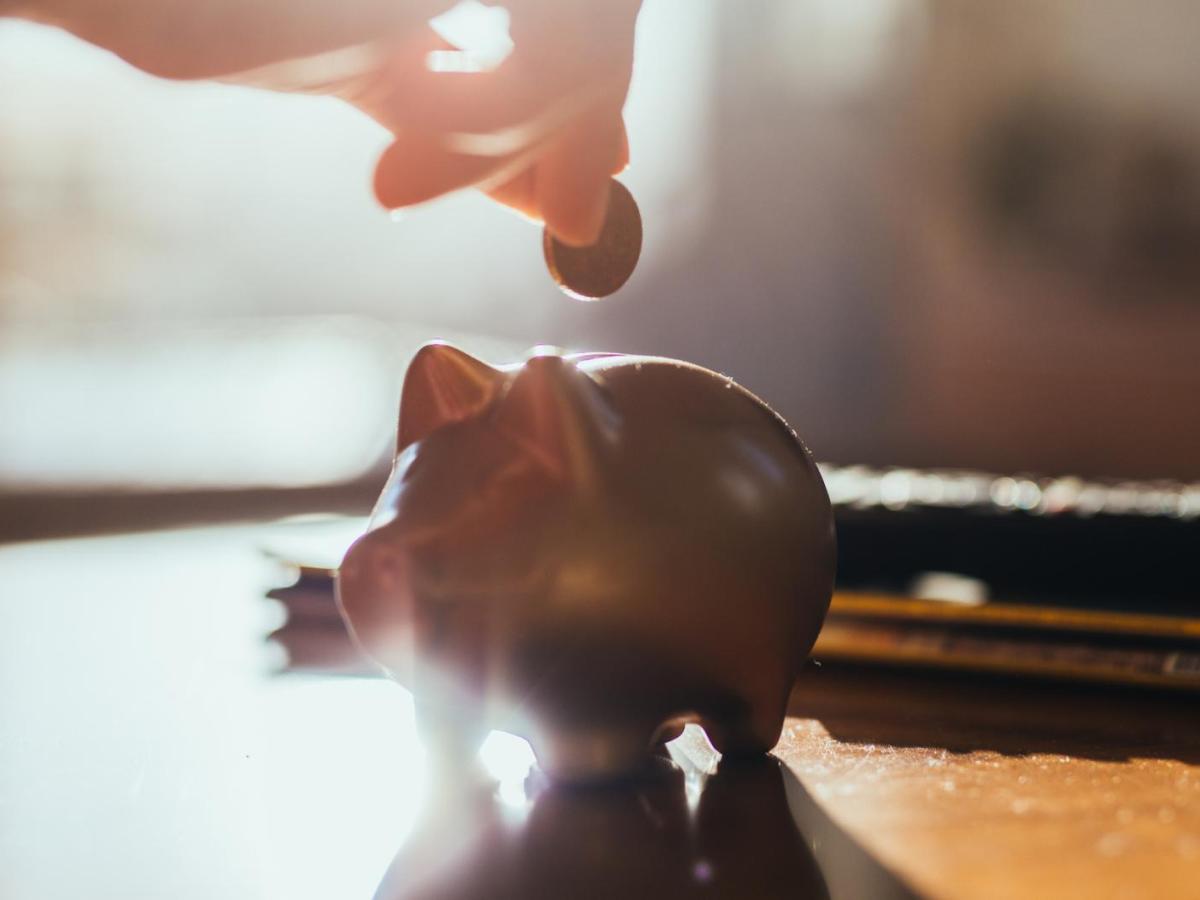 Person wirft eine Münze in ein goldenes Sparschwein.