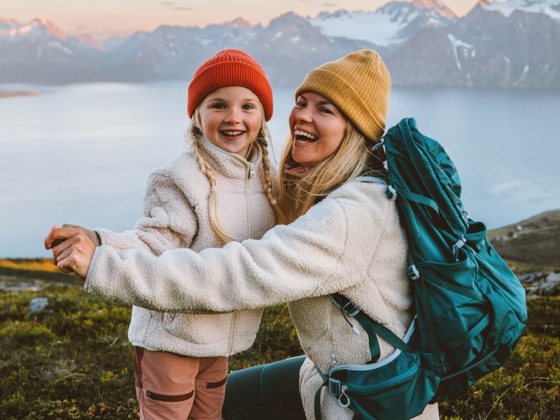 Mutter und Tochter in Outdoor Kleidung in einer bergigen Landschaft mit einem großen See im Hintergrund.