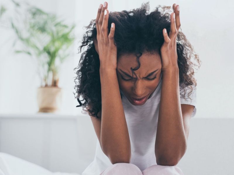 Erschöpfte afroamerikanische Frau leidet unter Kopfschmerzen im Schlafzimmer