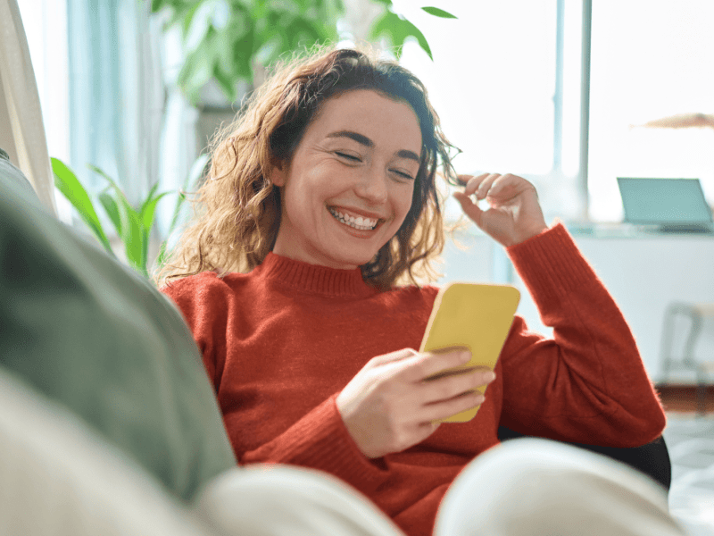 Junge Frau sitzt auf Sofa mit Handy in der Hand.