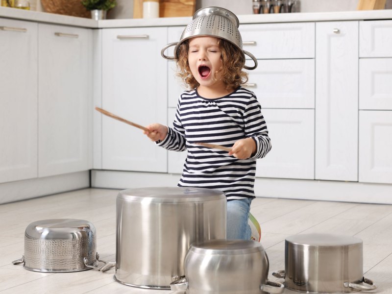 Kleines Mädchen, ca. 5 Jahre, tut so, als würde es auf Töpfen Schlagzeug spielen.