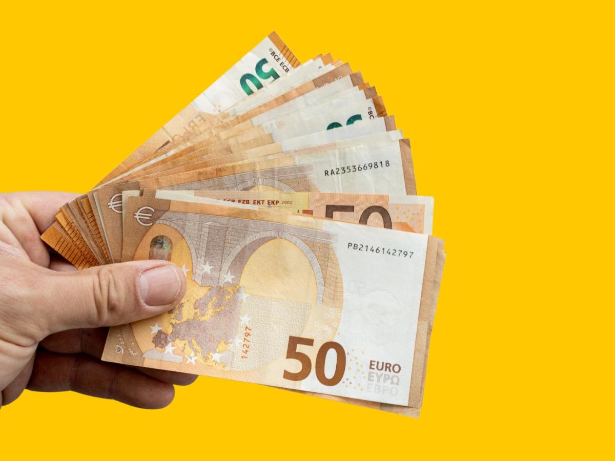 Eine Hand hält viele 50 Euro Scheine vor einem gelben Hintergrund.