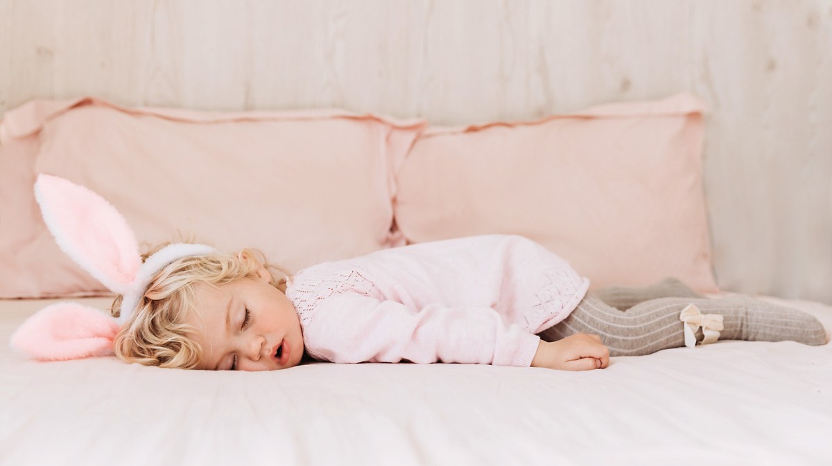 Kleines Mädchen, ca. 2 oder 3 Jahre alt, schläft mit Hasenohren auf dem Bett.