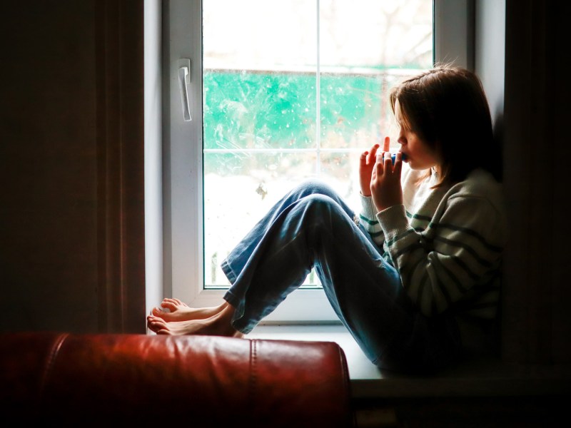 Mädchen sitzt alleine auf der Fensterbank und isst etwas.