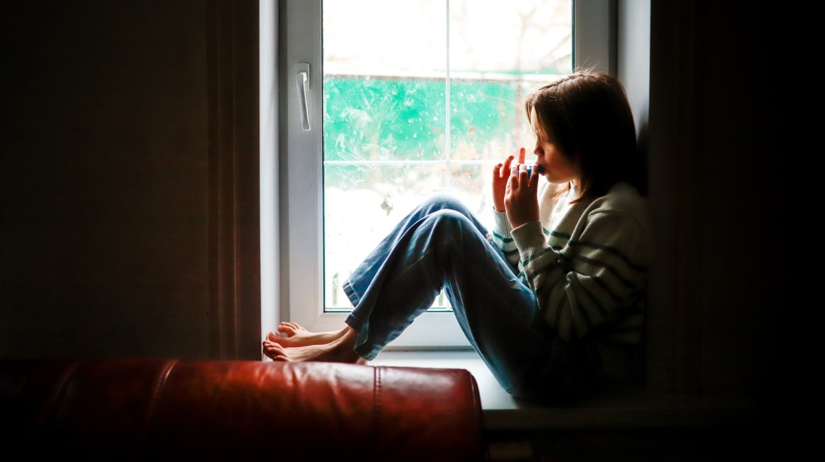 Mädchen sitzt alleine auf der Fensterbank und isst etwas.