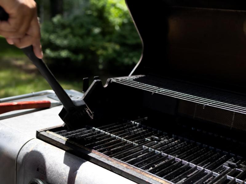 Person reinigt einen Grill mit einer Bürste.