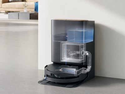 Die OMNI-Station spült die Wischwalze automatisch mit heißem Wasser und trocknet sie hygienisch – für dauerhaft saubere Reinigungsergebnisse ohne Geruchsbildung. Saugroboter an schwarzer Dockingstation mit transparent sichtbaren Wasser- und Schmutztanks, im hellen, stilvollen Wohnbereich.