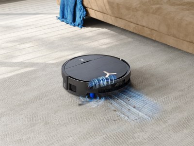 Schwarzer Saugroboter mit glänzender Oberfläche entfernt auf einem hellgrauen Teppich unter Sonnenlicht effektiv Staub und Haare.