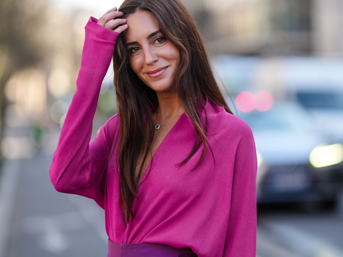 Brunette Frau mit pinker Bluse lächelt in die kamera, als Symbolbild für rosa Birkenstock Sandalen