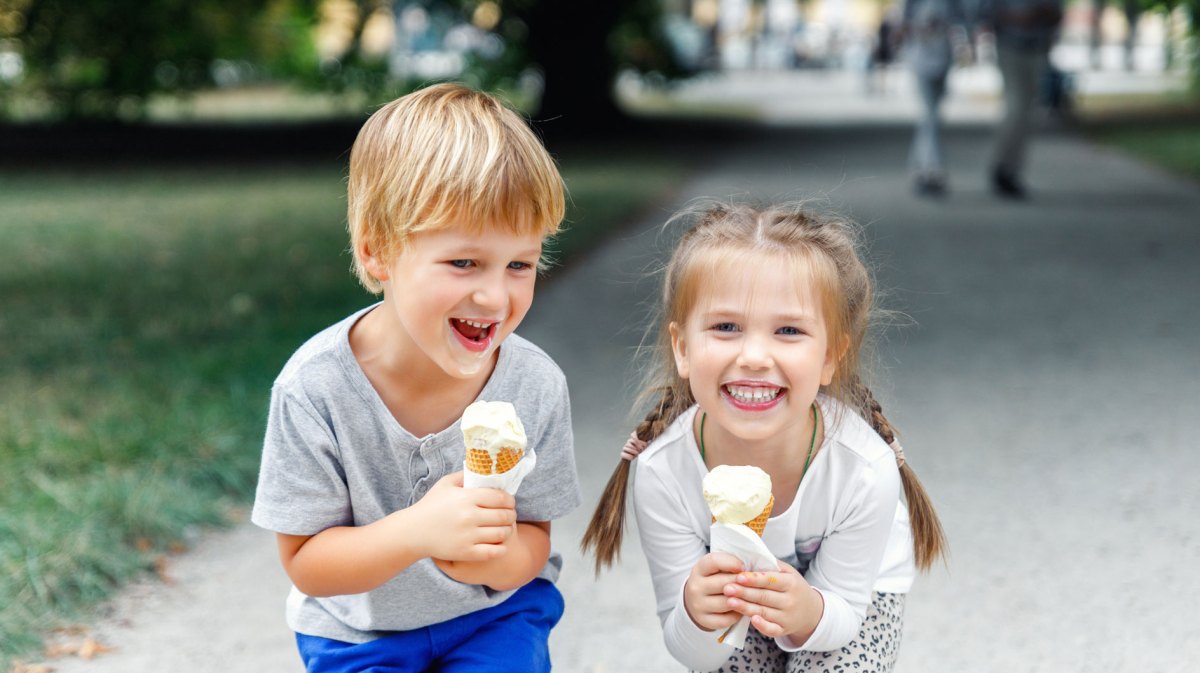 Porträt von zwei Kindern, einem Jungen und einem Mädchen, die draußen im Park sind und beide ein Eis in ihren Händen halten.