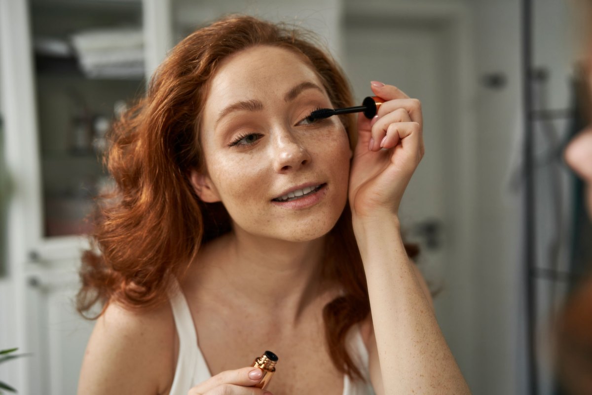 Frau, die sich mit einer Wimperntusche die Augen schminkt.