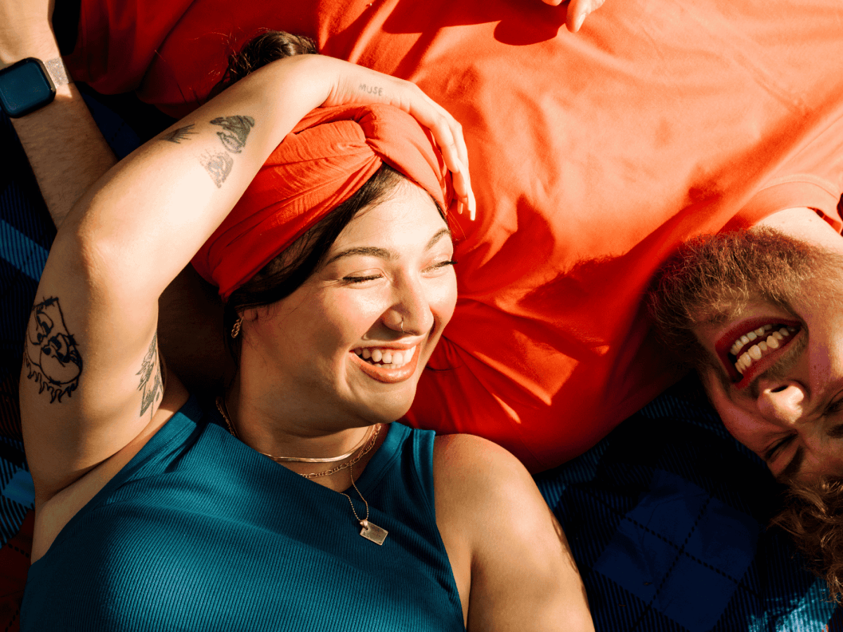 Frau mit orangenem Turban liegt lachend auf der Brust eines Mannes mit orangenem T-Shirt