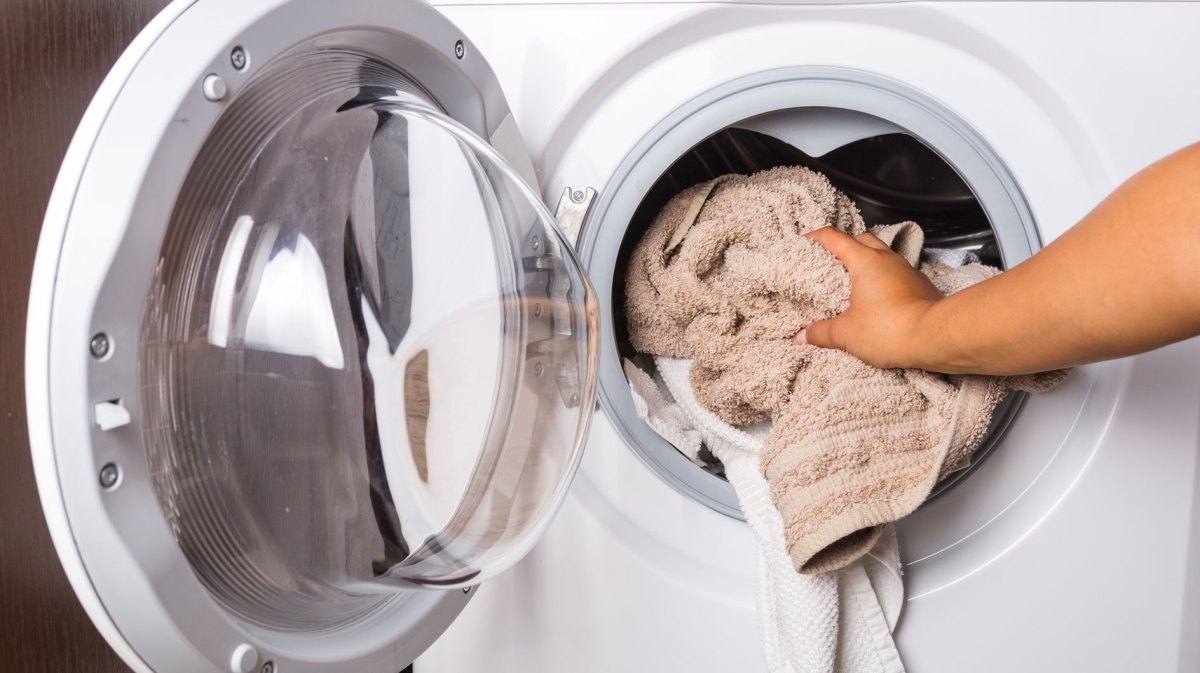 Hand gibt Handtücher in Waschmaschine
